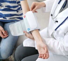 Photo of Doctor checking woman's heart rate and blood pressure via sphygmomanometer on sofa indoors, closeup