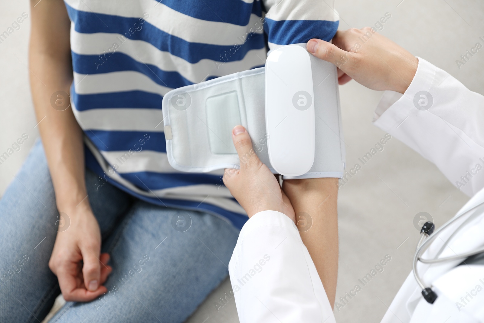 Doctor checking woman's heart rate and blood pressure via sphygmomanometer on sofa indoors, closeup Photo of Doctor checking woman's heart rate and blood pressure via sphygmomanometer on sofa indoors, closeup