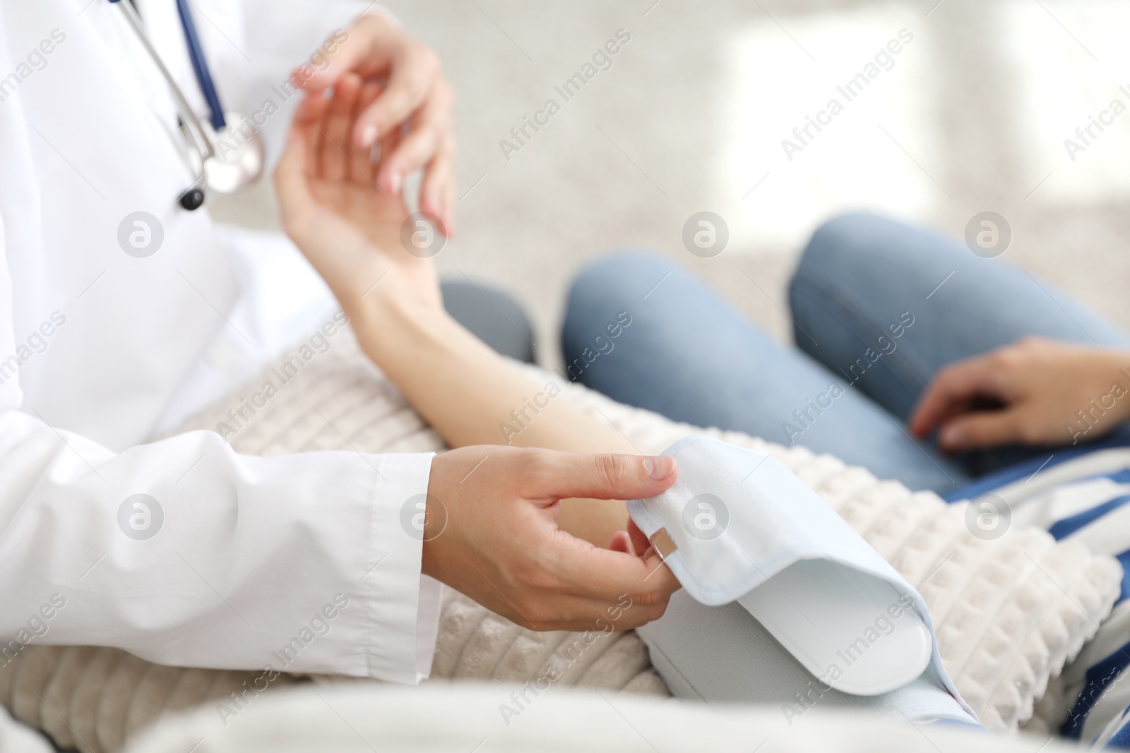 Photo of Doctor checking woman's heart rate and blood pressure via sphygmomanometer on sofa indoors, closeup