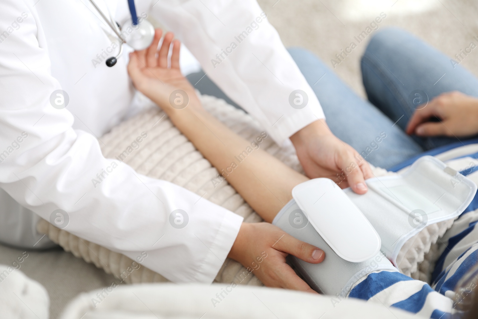 Doctor checking woman's heart rate and blood pressure via sphygmomanometer on sofa indoors, closeup Photo of Doctor checking woman's heart rate and blood pressure via sphygmomanometer on sofa indoors, closeup