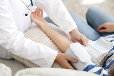 Photo of Doctor checking woman's heart rate and blood pressure via sphygmomanometer on sofa indoors, closeup