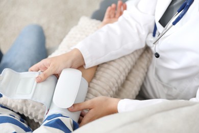 Photo of Doctor checking woman's heart rate and blood pressure via sphygmomanometer on sofa indoors, closeup