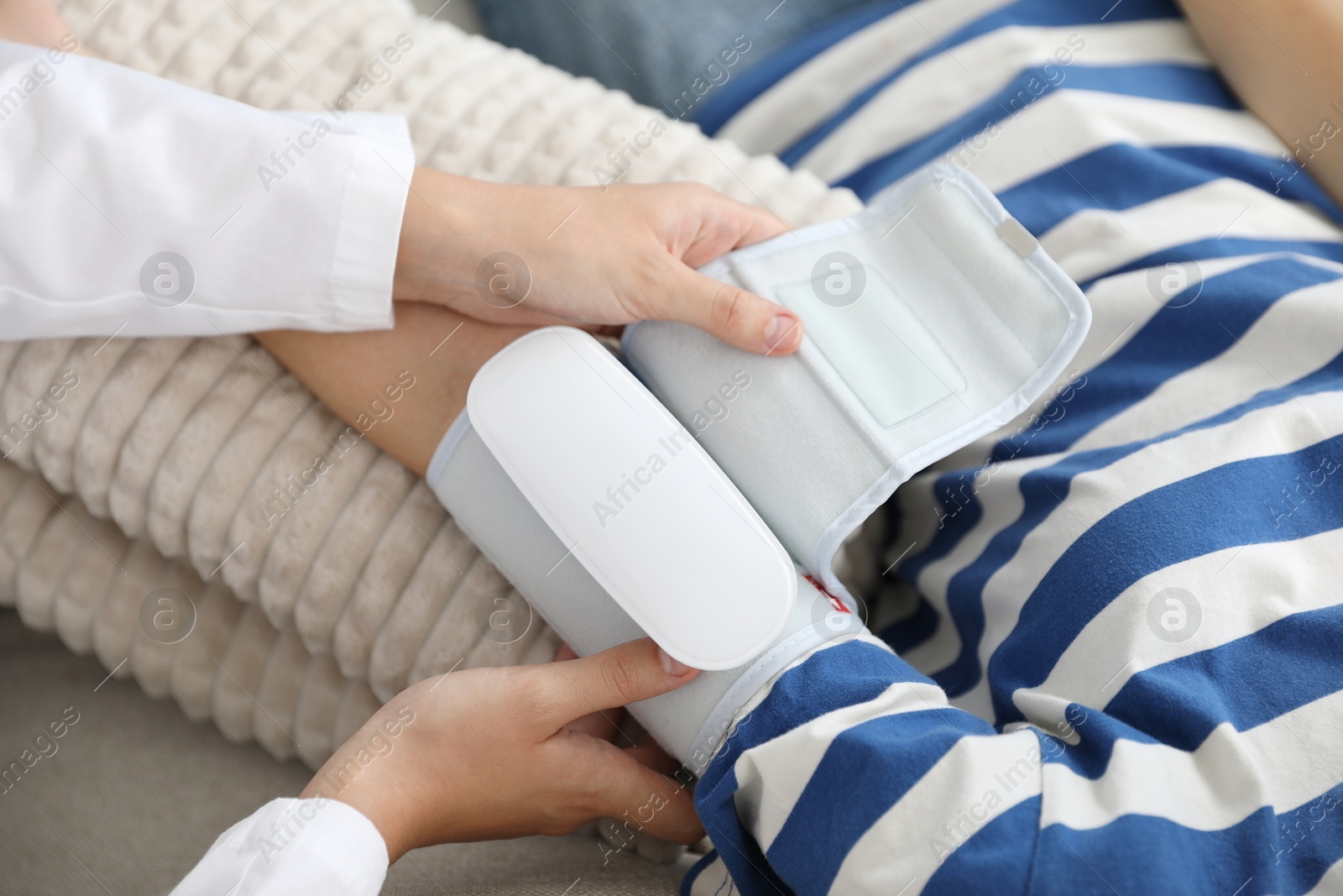 Doctor checking woman's heart rate and blood pressure via sphygmomanometer on sofa indoors, closeup Photo of Doctor checking woman's heart rate and blood pressure via sphygmomanometer on sofa indoors, closeup