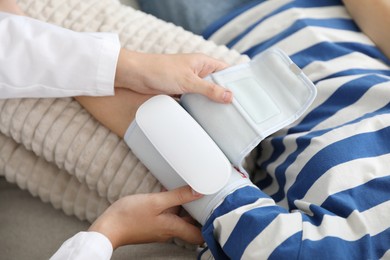 Photo of Doctor checking woman's heart rate and blood pressure via sphygmomanometer on sofa indoors, closeup