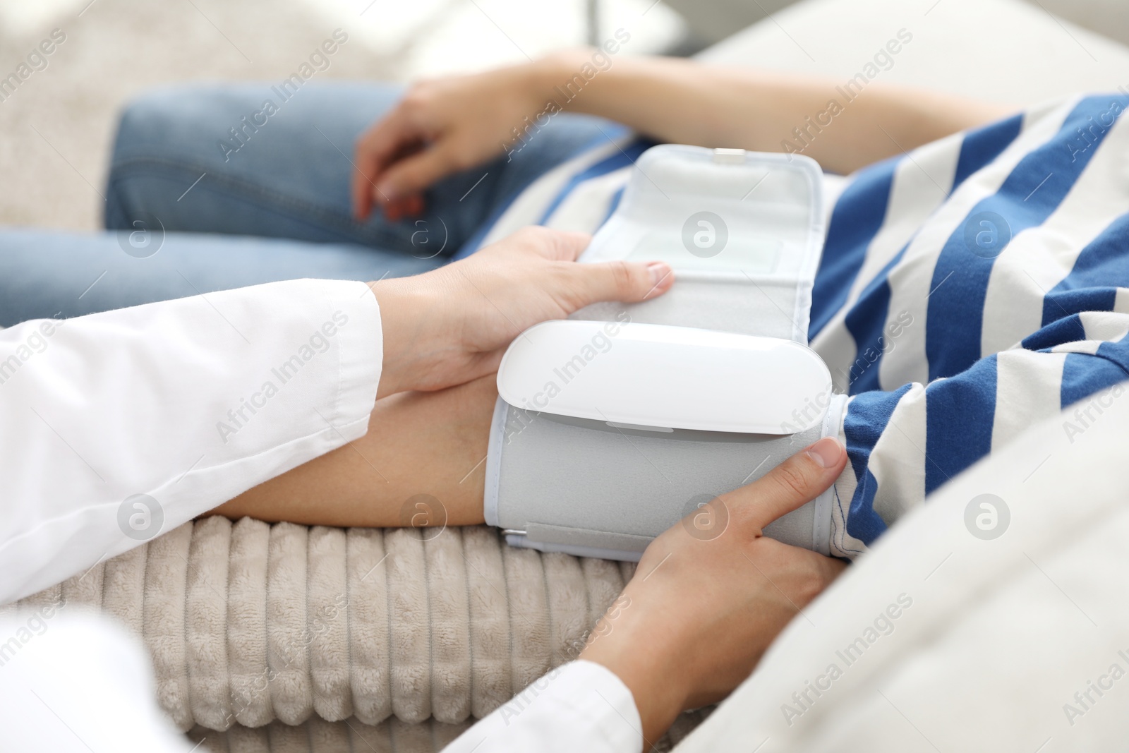 Doctor checking woman's heart rate and blood pressure via sphygmomanometer on sofa indoors, closeup Photo of Doctor checking woman's heart rate and blood pressure via sphygmomanometer on sofa indoors, closeup