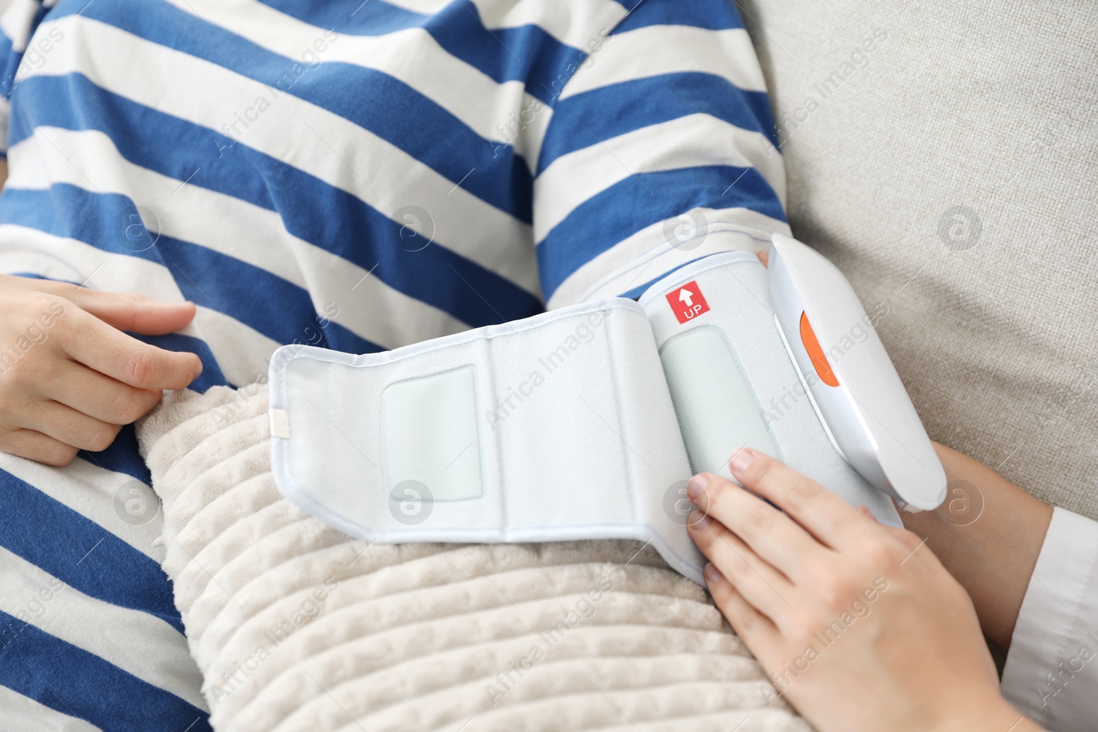 Doctor checking woman's heart rate and blood pressure via sphygmomanometer on sofa indoors, closeup Photo of Doctor checking woman's heart rate and blood pressure via sphygmomanometer on sofa indoors, closeup