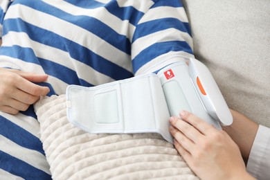 Photo of Doctor checking woman's heart rate and blood pressure via sphygmomanometer on sofa indoors, closeup