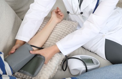 Photo of Doctor checking woman's heart rate and blood pressure via sphygmomanometer on sofa indoors, closeup