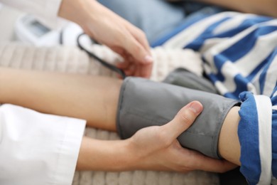 Photo of Doctor checking woman's heart rate and blood pressure via sphygmomanometer on sofa indoors, closeup