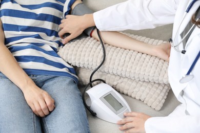 Photo of Doctor checking woman's heart rate and blood pressure via sphygmomanometer on sofa indoors, closeup