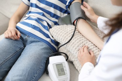 Photo of Doctor checking woman's heart rate and blood pressure via sphygmomanometer on sofa indoors, closeup