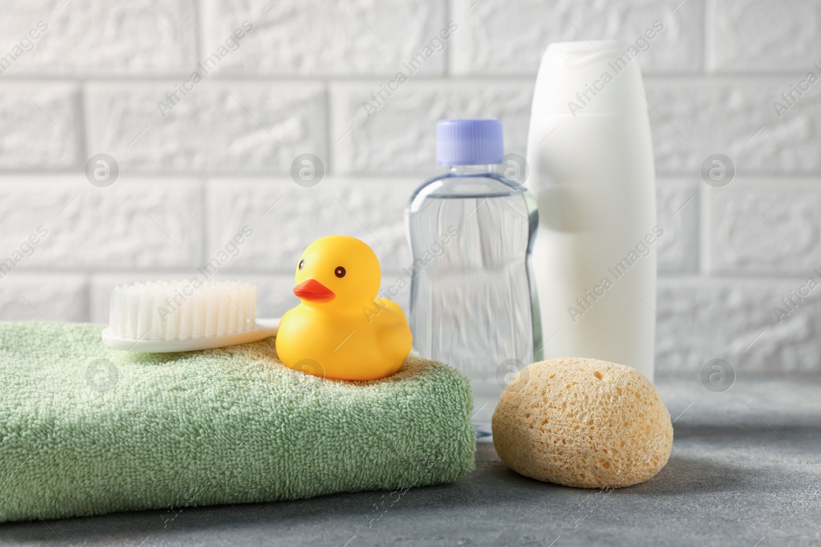 Photo of Baby bath accessories and care products on grey table against white brick wall, closeup