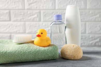 Photo of Baby bath accessories and care products on grey table against white brick wall, closeup