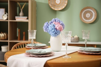 Photo of Stylish setting with plates and vase of flowers on wooden table in dining room. Interior design