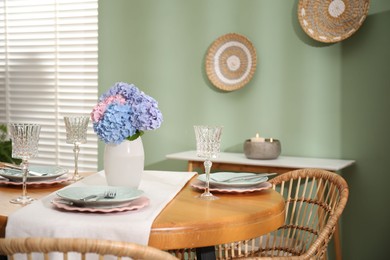 Photo of Stylish setting with plates and vase of flowers on wooden table in dining room. Interior design