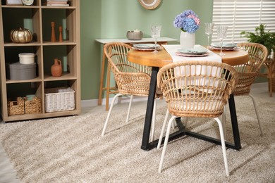 Photo of Stylish setting with plates and vase of flowers on wooden table in dining room. Interior design
