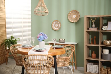 Photo of Stylish setting with plates and vase of flowers on wooden table in dining room. Interior design