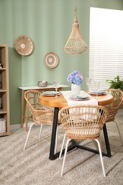 Photo of Stylish setting with plates and vase of flowers on wooden table in dining room. Interior design