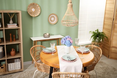 Photo of Stylish setting with plates and vase of flowers on wooden table in dining room. Interior design
