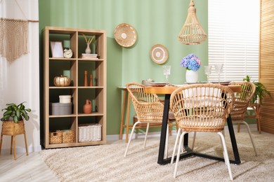 Photo of Stylish setting with plates and vase of flowers on wooden table in dining room. Interior design