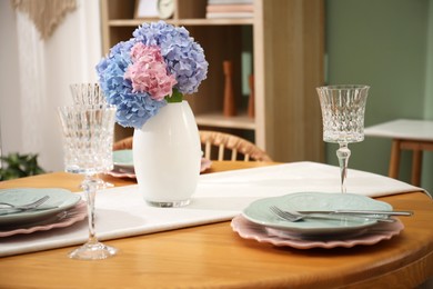 Photo of Stylish setting with plates and vase of flowers on wooden table in dining room. Interior design