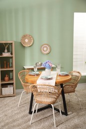 Photo of Stylish setting with plates and vase of flowers on wooden table in dining room. Interior design