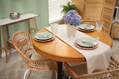 Photo of Stylish setting with plates and vase of flowers on wooden table in dining room. Interior design