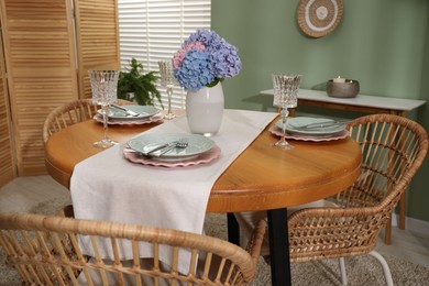 Photo of Stylish setting with plates and vase of flowers on wooden table in dining room. Interior design