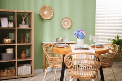 Photo of Stylish setting with plates and vase of flowers on wooden table in dining room. Interior design
