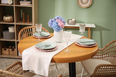 Photo of Stylish setting with plates and vase of flowers on wooden table in dining room. Interior design