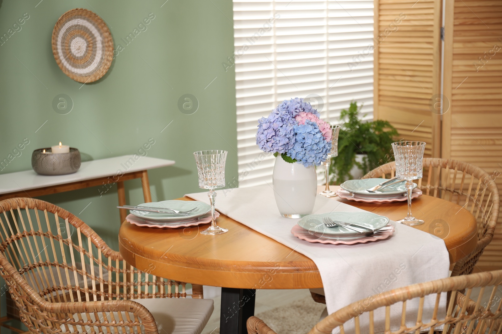 Photo of Stylish setting with plates and vase of flowers on wooden table in dining room. Interior design