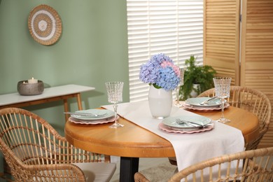 Photo of Stylish setting with plates and vase of flowers on wooden table in dining room. Interior design