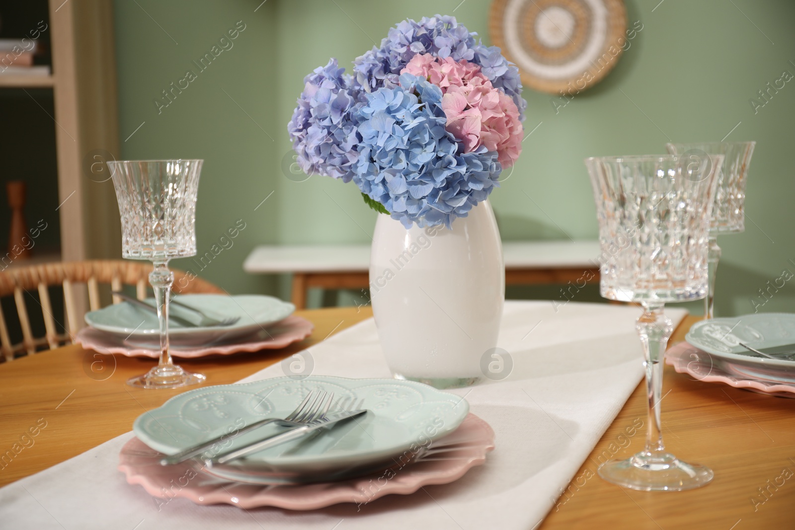 Photo of Stylish setting with plates and vase of flowers on wooden table in dining room, closeup. Interior design
