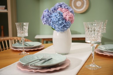 Photo of Stylish setting with plates and vase of flowers on wooden table in dining room, closeup. Interior design