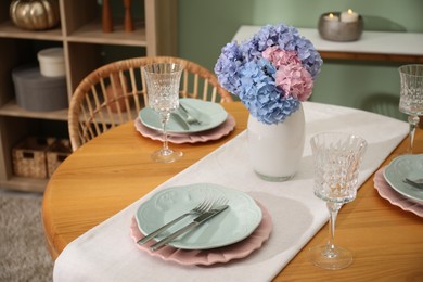 Photo of Stylish setting with plates and vase of flowers on wooden table in dining room. Interior design