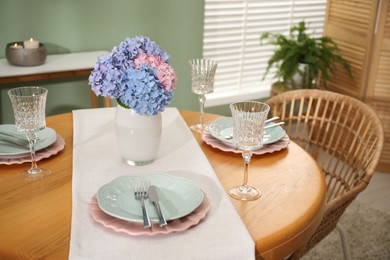 Photo of Stylish setting with plates and vase of flowers on wooden table in dining room. Interior design