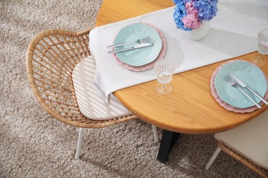 Photo of Stylish setting with plates and vase of flowers on wooden table in dining room, above view. Interior design