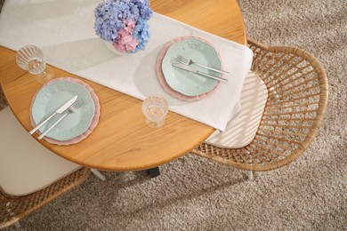 Photo of Stylish setting with plates and vase of flowers on wooden table in dining room, above view. Interior design