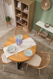 Photo of Stylish setting with plates and vase of flowers on wooden table in dining room, above view. Interior design