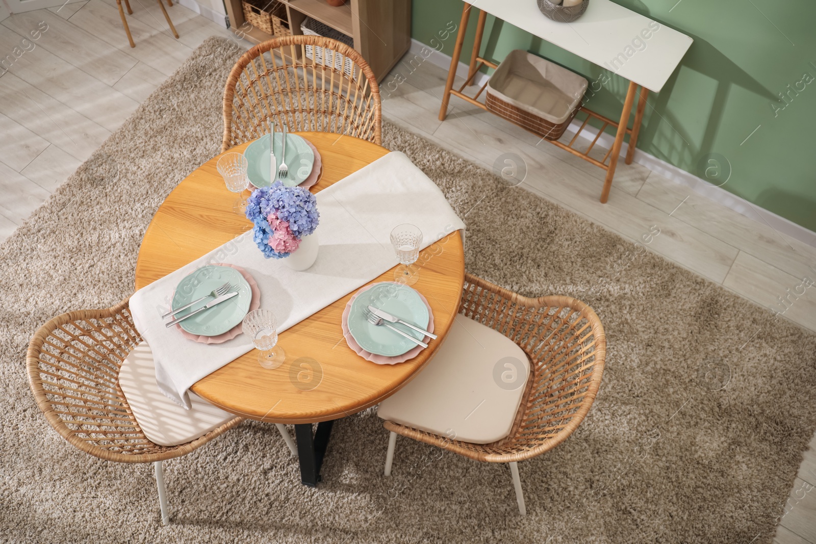 Photo of Stylish setting with plates and vase of flowers on wooden table in dining room, above view. Interior design