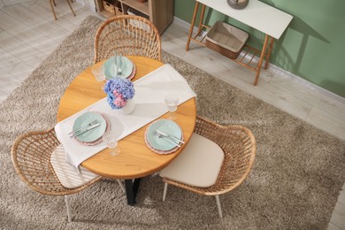 Photo of Stylish setting with plates and vase of flowers on wooden table in dining room, above view. Interior design