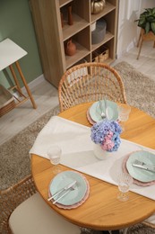 Photo of Stylish setting with plates and vase of flowers on wooden table in dining room, above view. Interior design