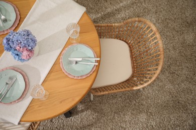 Photo of Stylish setting with plates and vase of flowers on wooden table in dining room, above view. Interior design