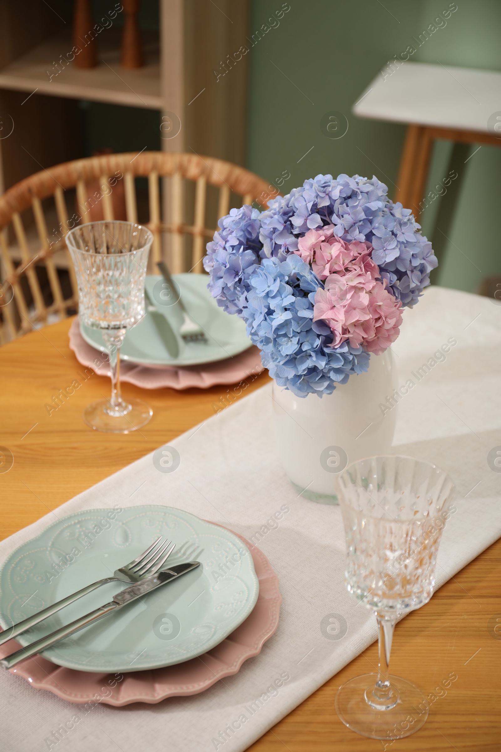 Photo of Stylish setting with plates and vase of flowers on wooden table in dining room. Interior design