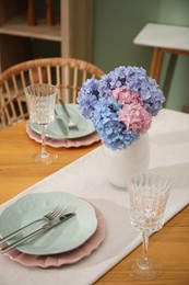 Photo of Stylish setting with plates and vase of flowers on wooden table in dining room. Interior design