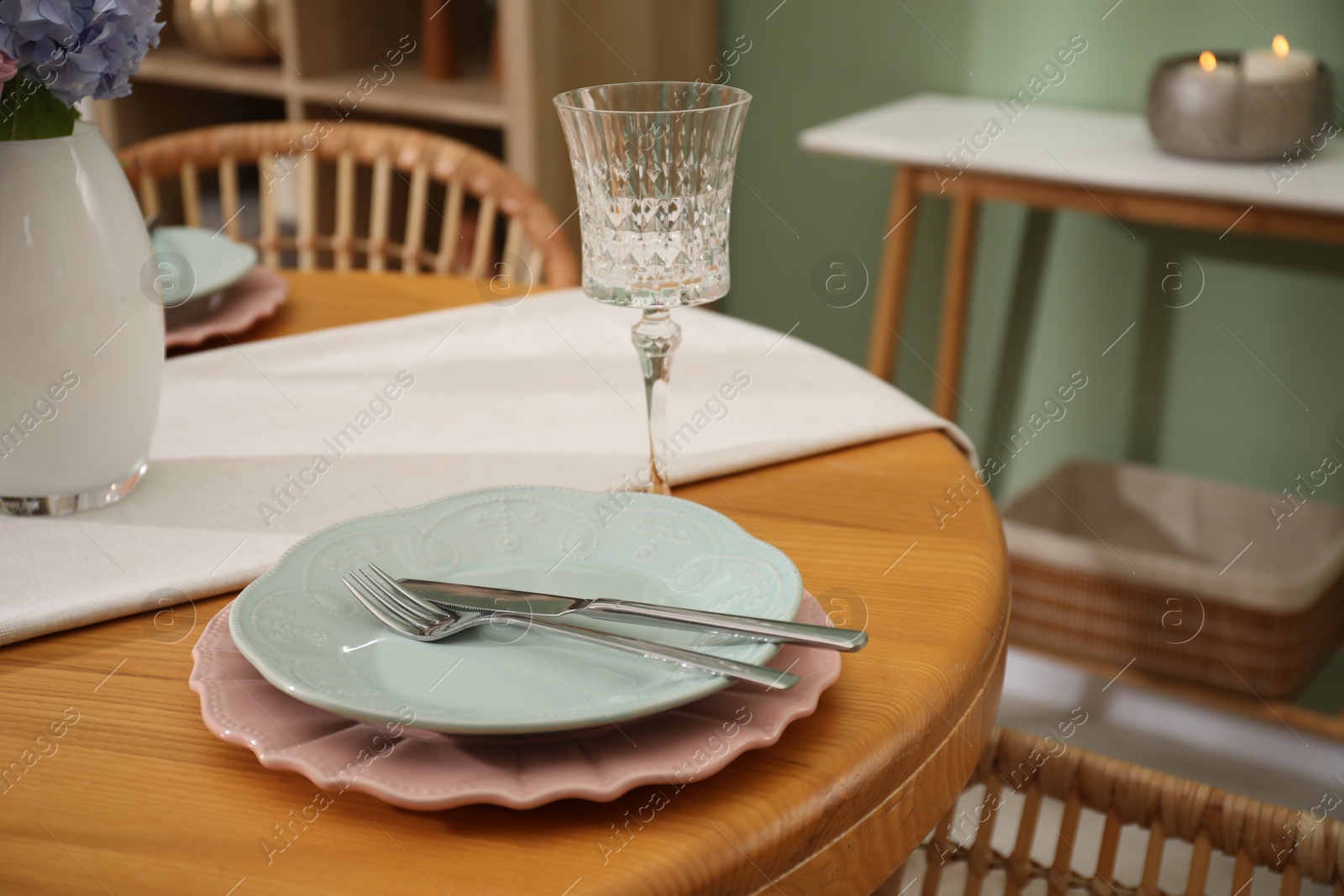 Photo of Stylish setting with plates and vase of flowers on wooden table in dining room, closeup. Interior design