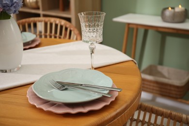 Photo of Stylish setting with plates and vase of flowers on wooden table in dining room, closeup. Interior design