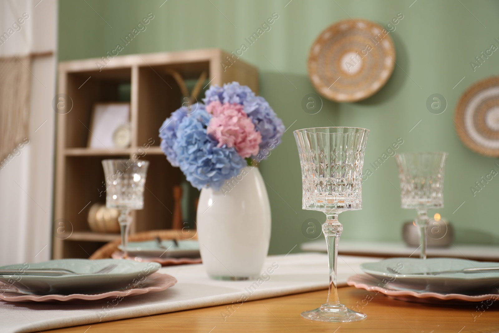 Photo of Stylish setting with plates and vase of flowers on wooden table in dining room. Interior design