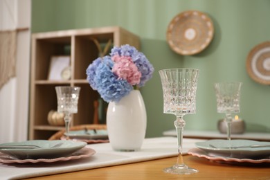 Photo of Stylish setting with plates and vase of flowers on wooden table in dining room. Interior design