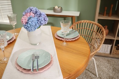 Photo of Stylish setting with plates and vase of flowers on wooden table in dining room. Interior design